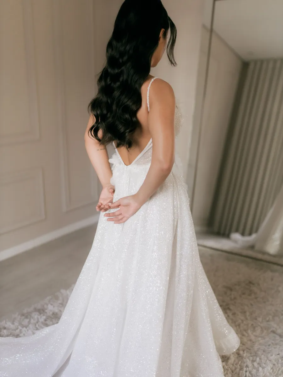 A bride in her finished gown seen from behind, facing a mirror