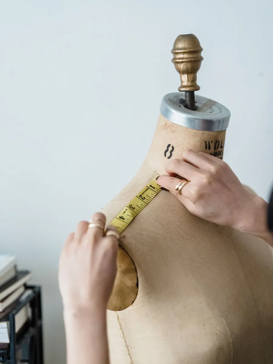 A fitter measures a dress form with a tape