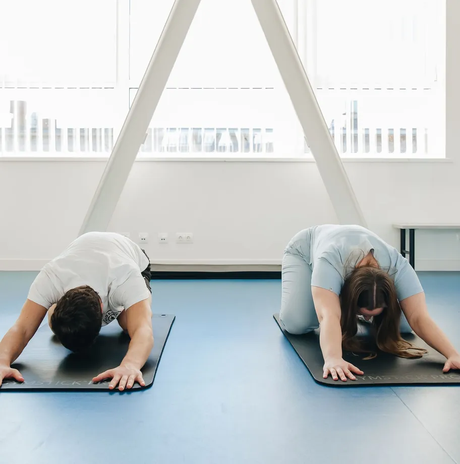 Two people stretching on mats by a large window