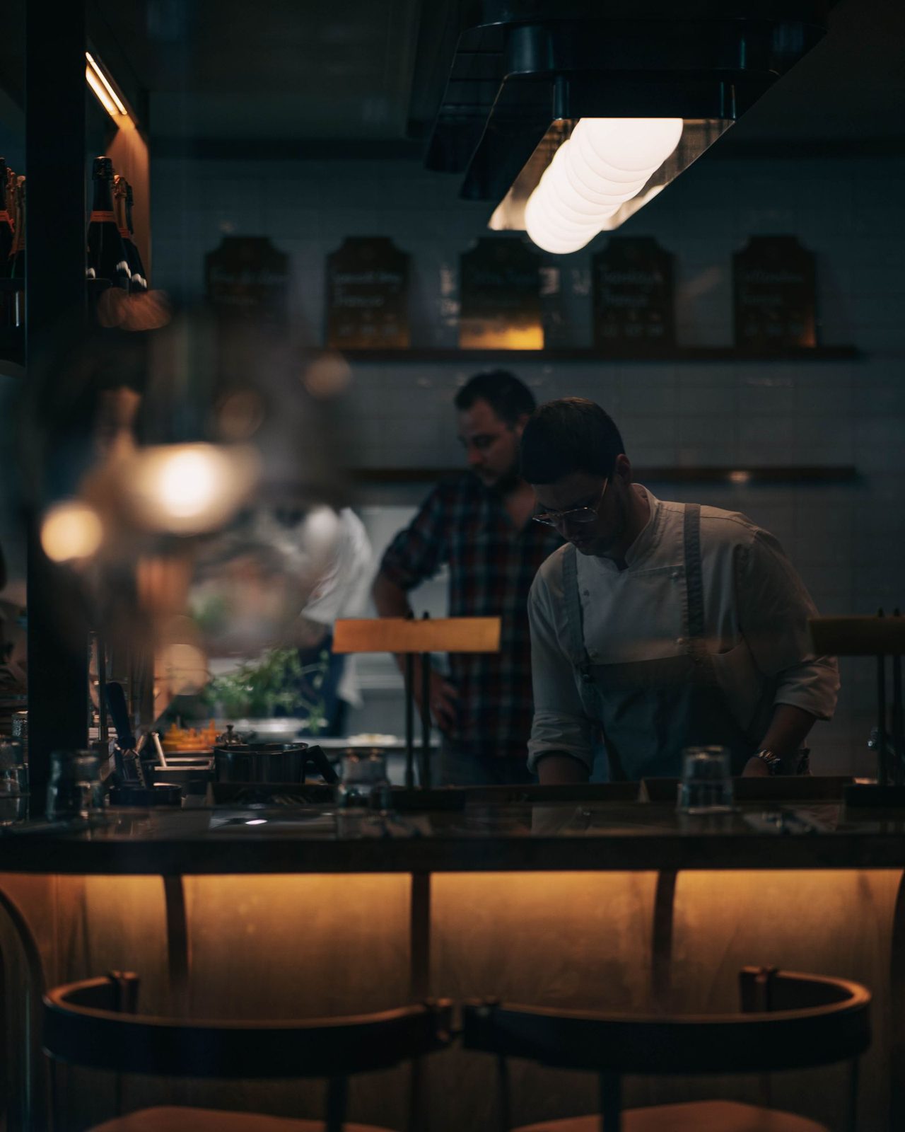 Cooks working behind a glowing bar counter at night