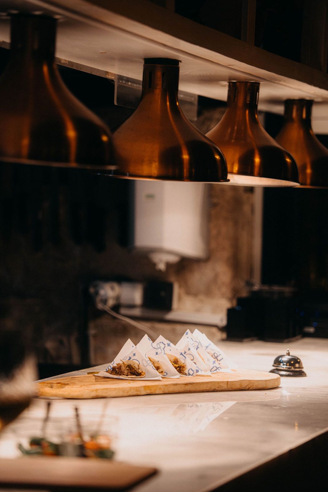 Copper pendant lamps glowing over a stone counter with dumplings waiting on a board
