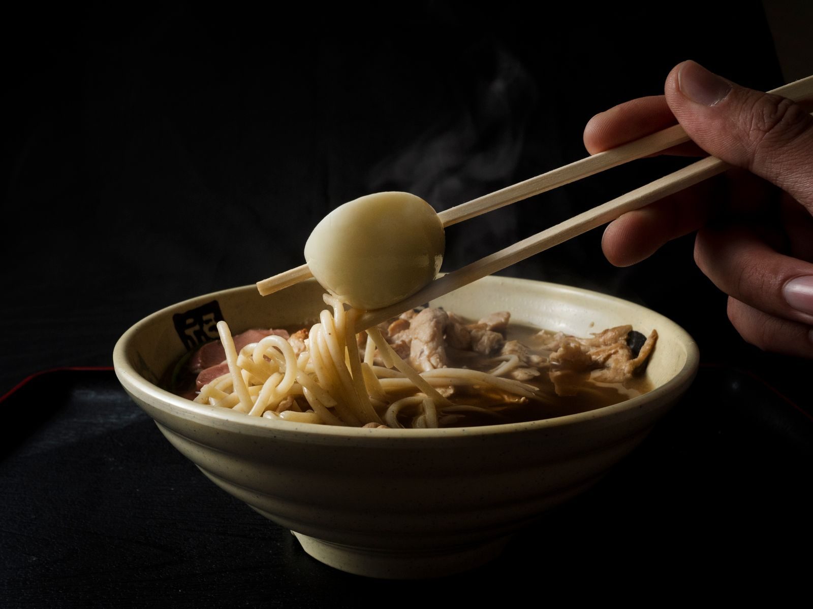 Chopsticks lifting an egg and noodles out of a bowl of ramen