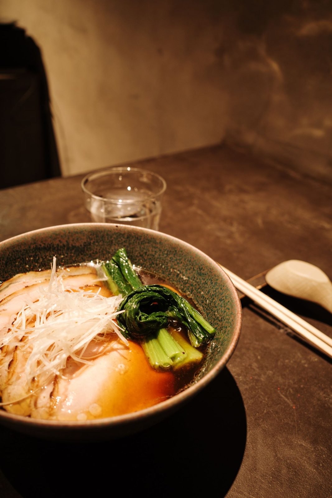 Bowl of chashu ramen with greens and a soft egg in low light
