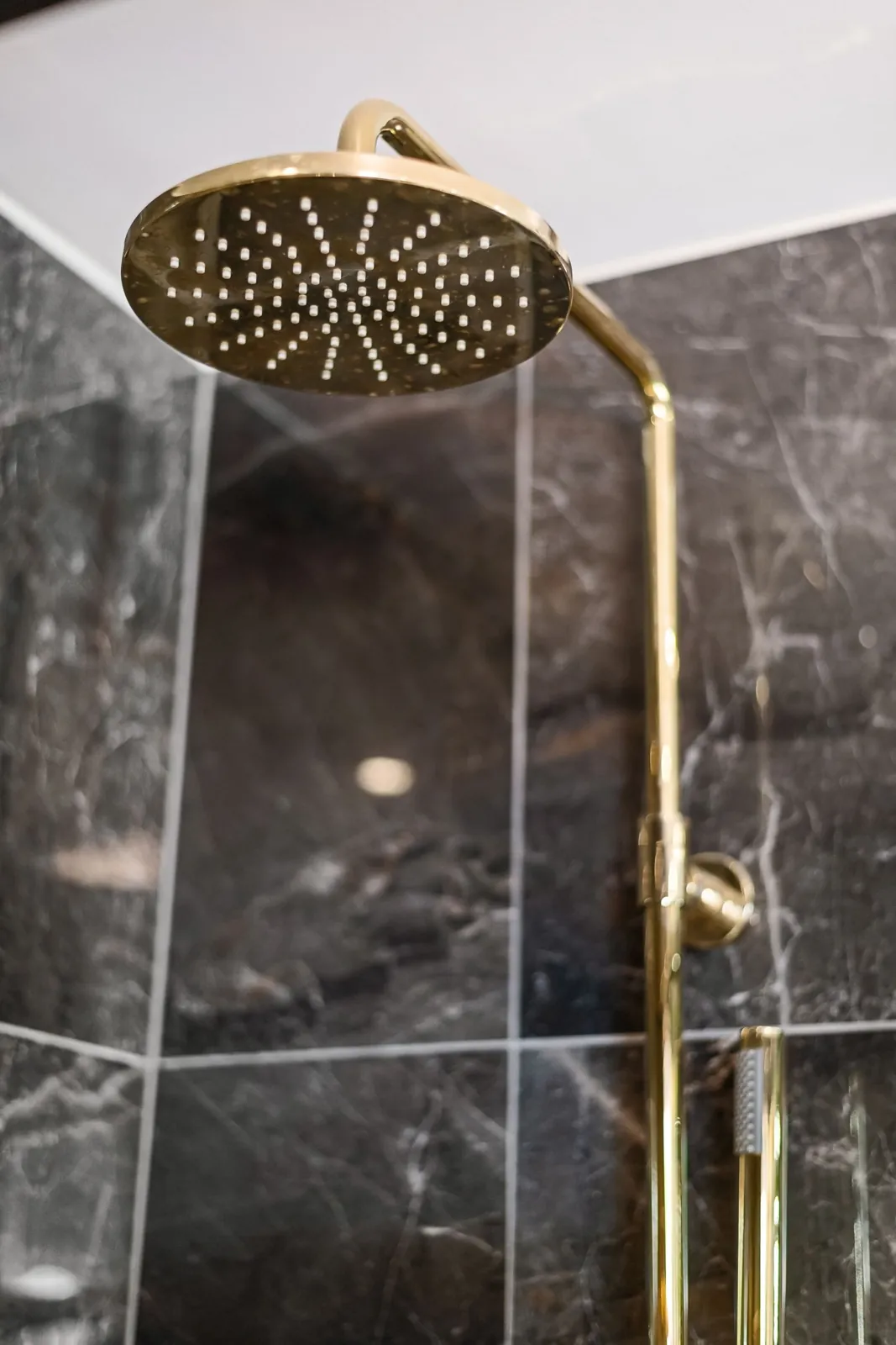 A marble shower with a brass rain head